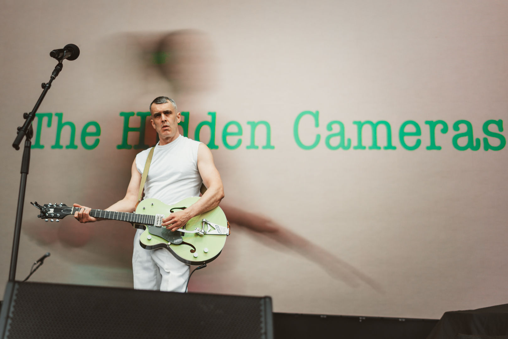 Musician in white outfit playing guitar on stage with blurred background