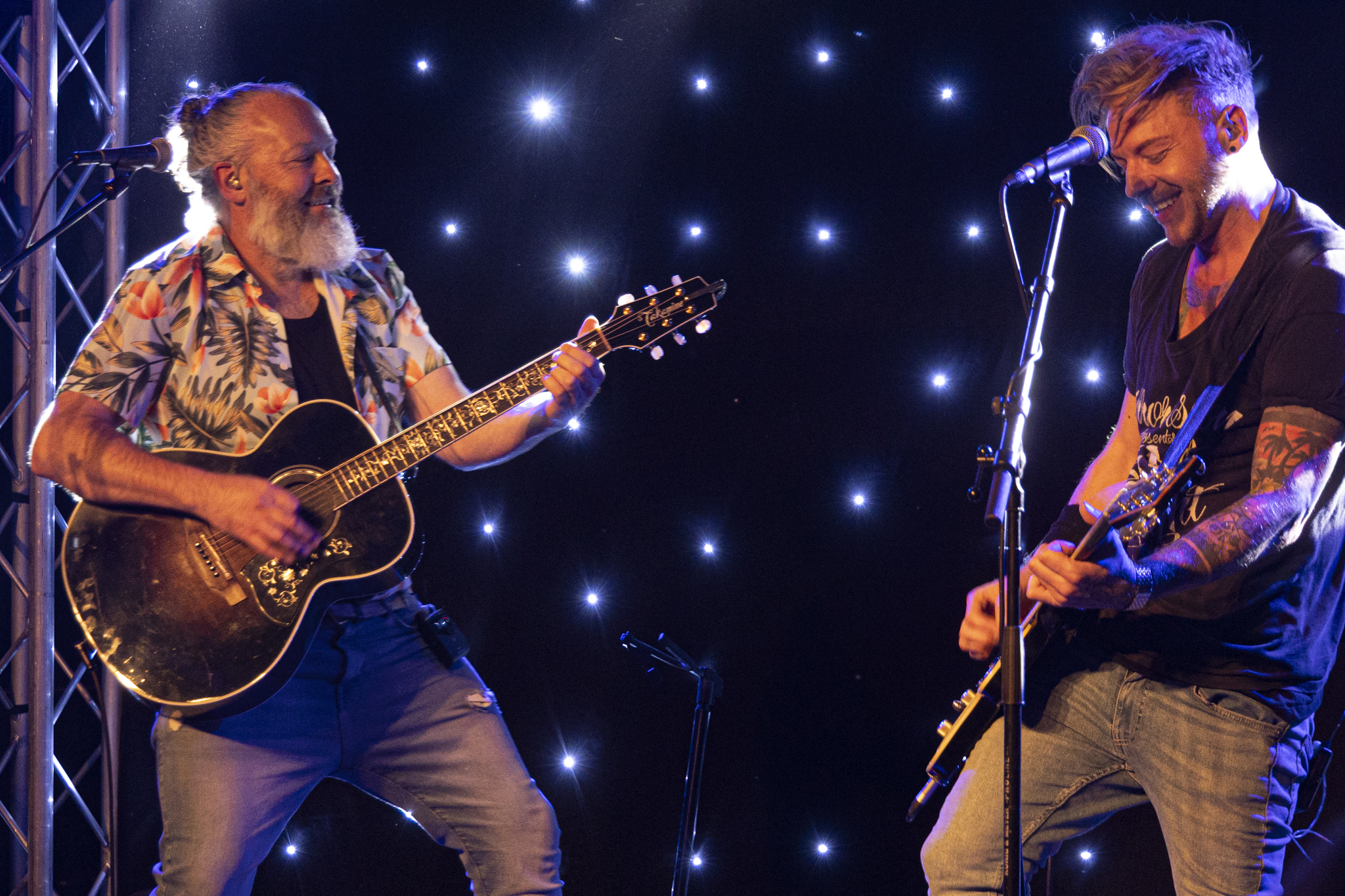 Two musicians playing guitars on stage with starry backdrop