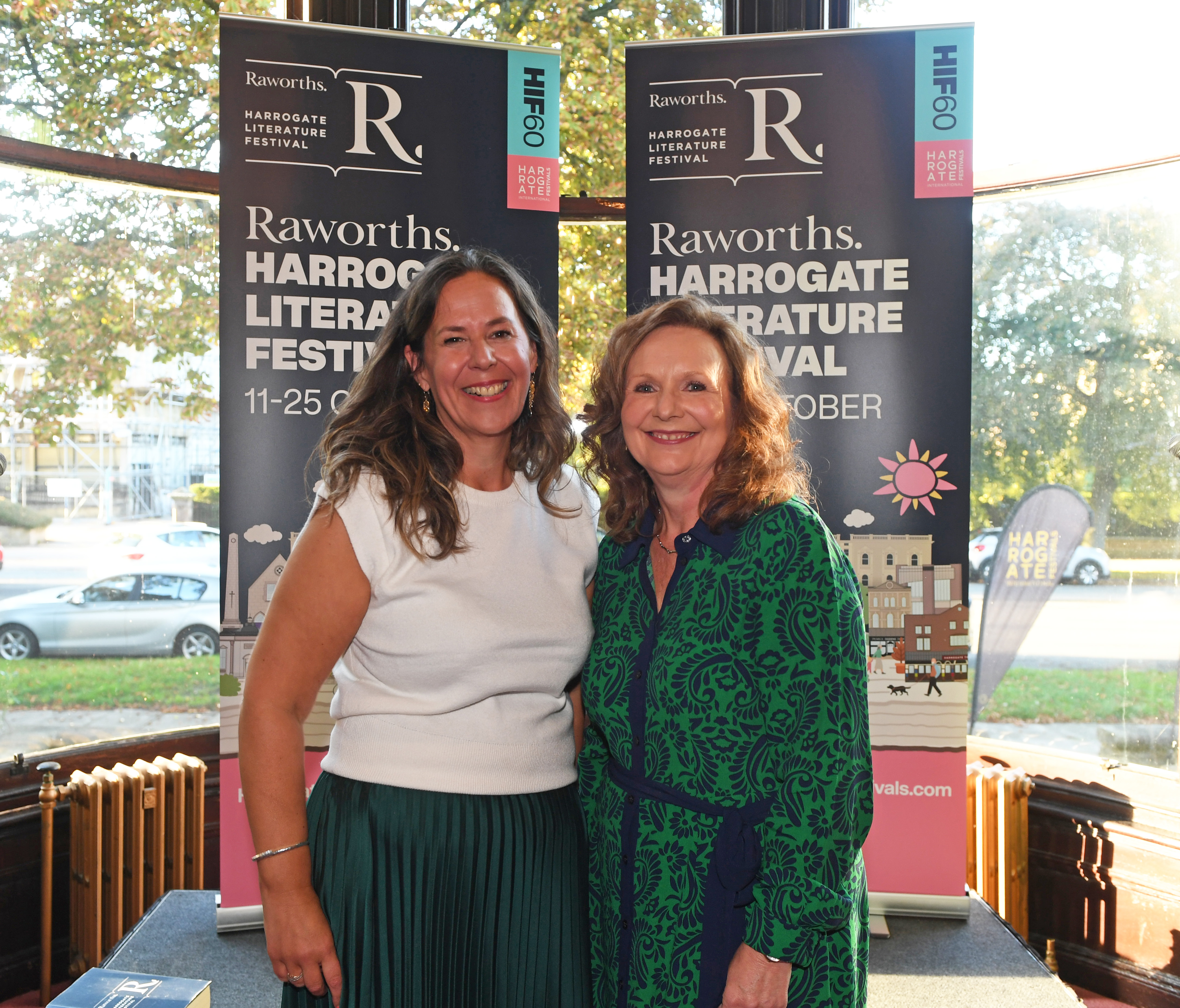Two women smiling in front of Harrogate Literature Festival banners