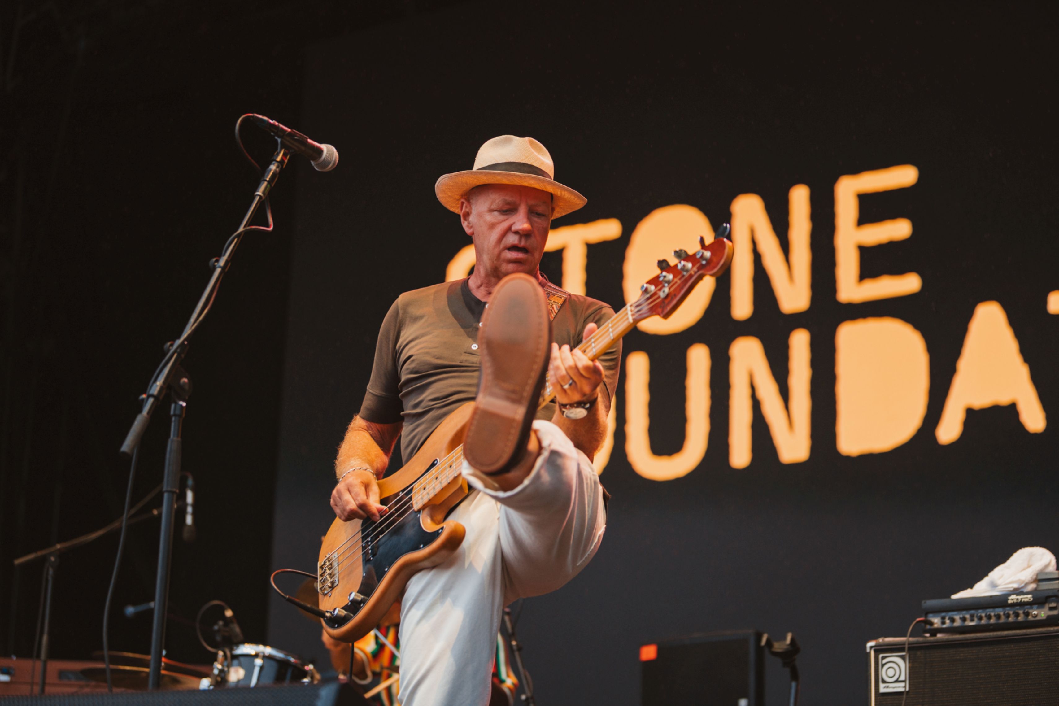 Musician on stage playing bass guitar wearing a hat and white trousers