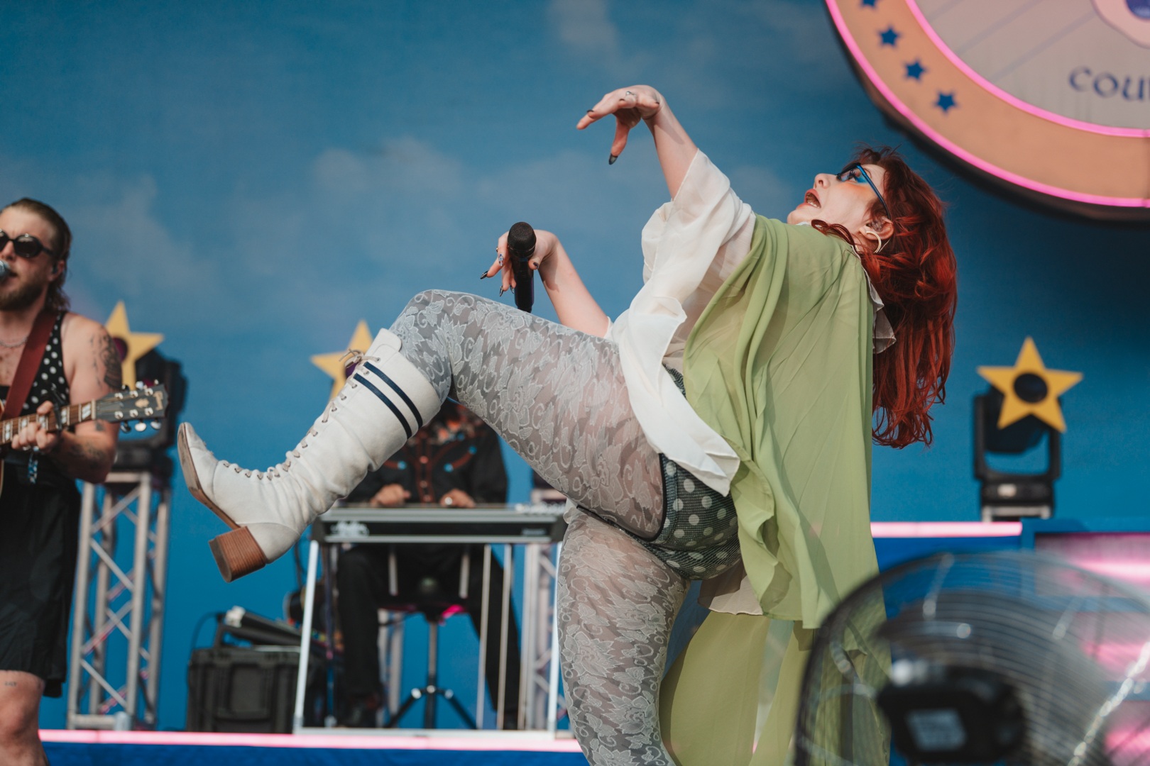 Performer in green cape and white boots dancing energetically on stage