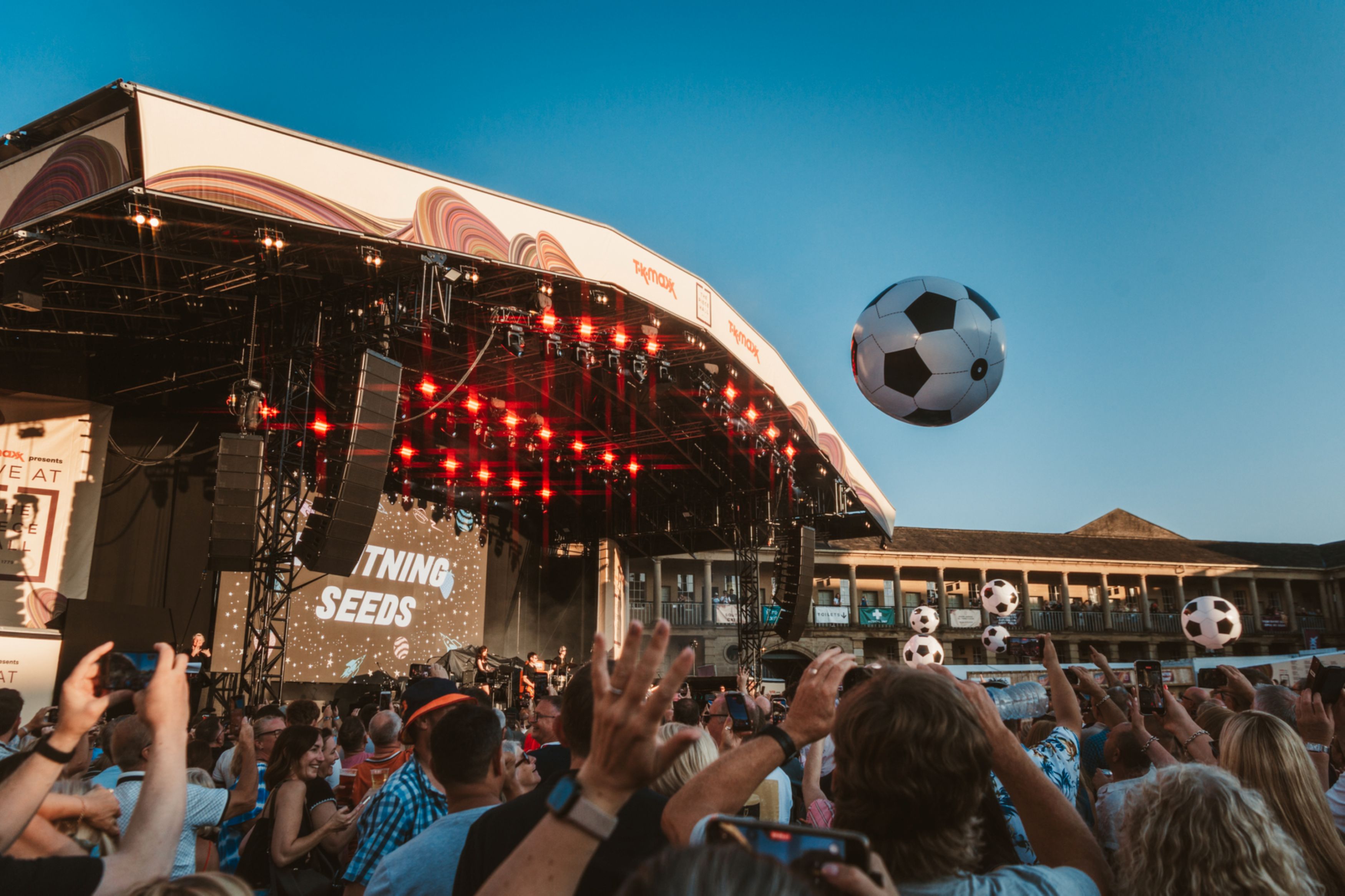 Crowd enjoying outdoor concert with soccer balls in the air
