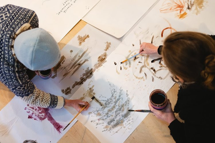 Two people painting abstract watercolours on large paper sheets