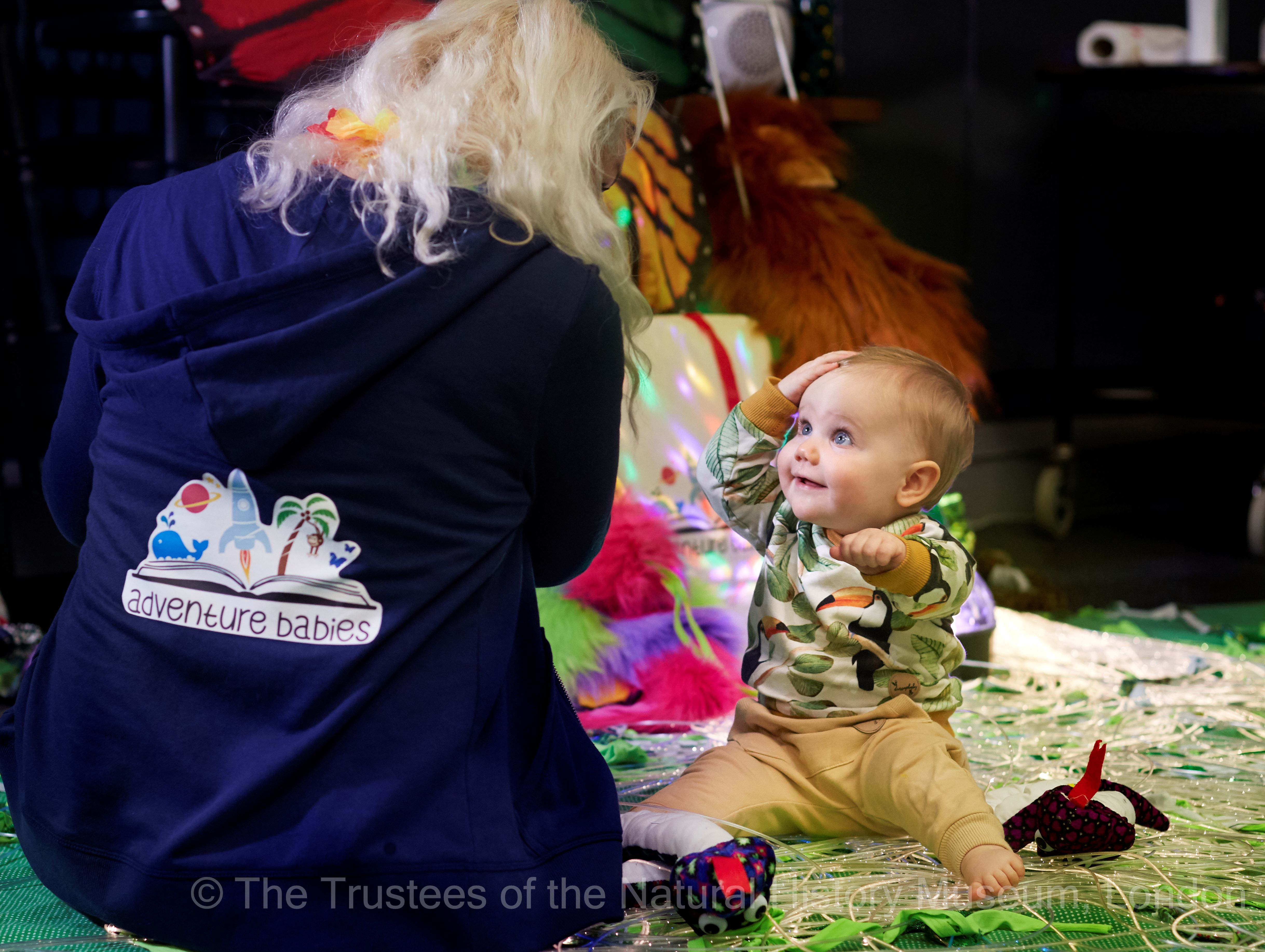 Baby playing on colorful mat with adult in adventure hoodie