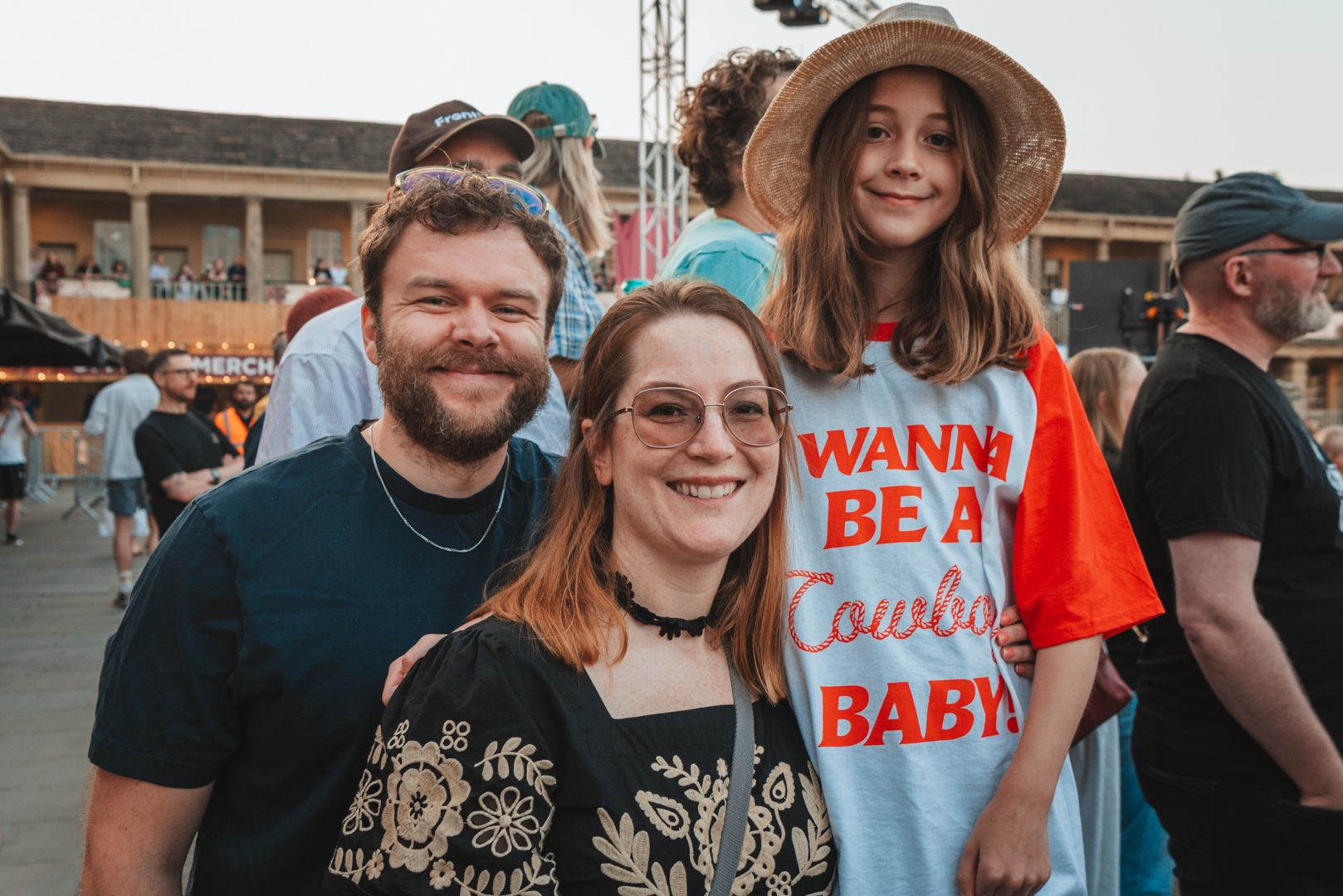 Family smiling at an outdoor event with people and stalls