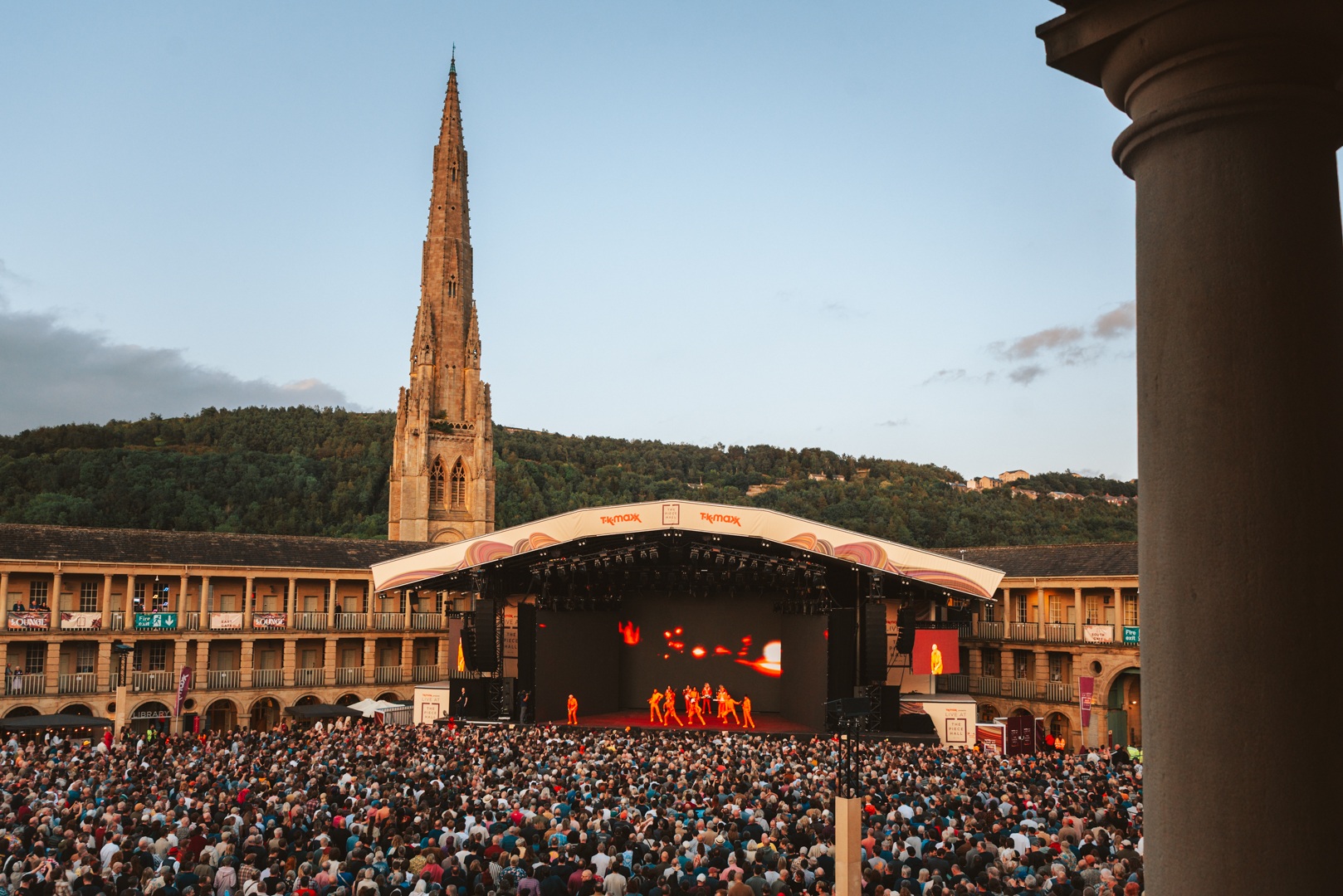 Large outdoor concert with crowd and illuminated stage in front of historic spire