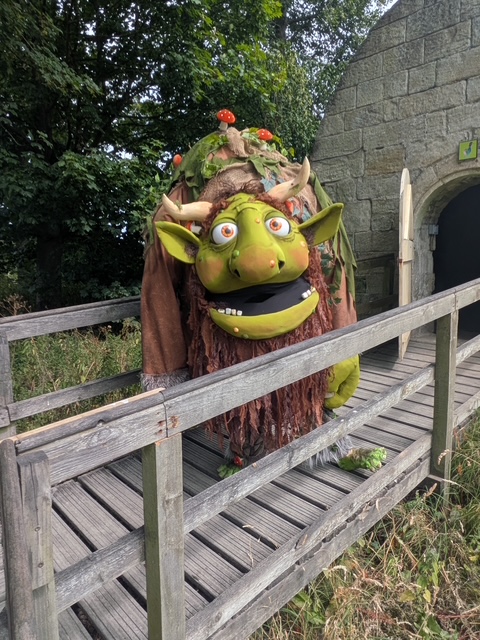 Large green troll sculpture with horns and foliage near stone building
