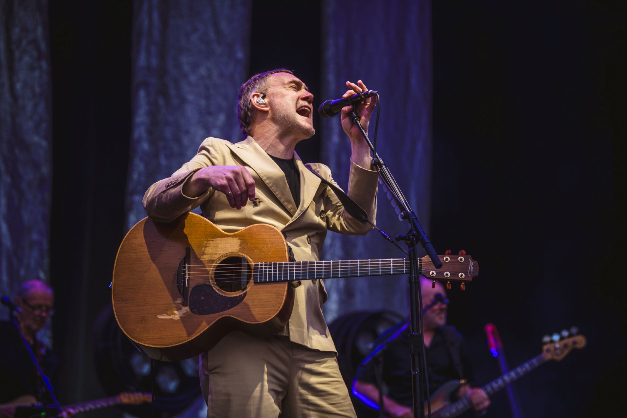 Musician in beige suit playing guitar on stage with band