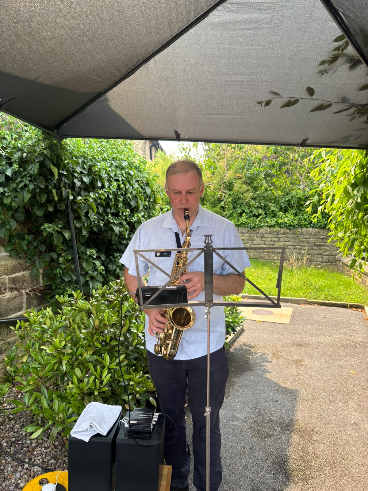 Man playing saxophone under garden canopy surrounded by greenery