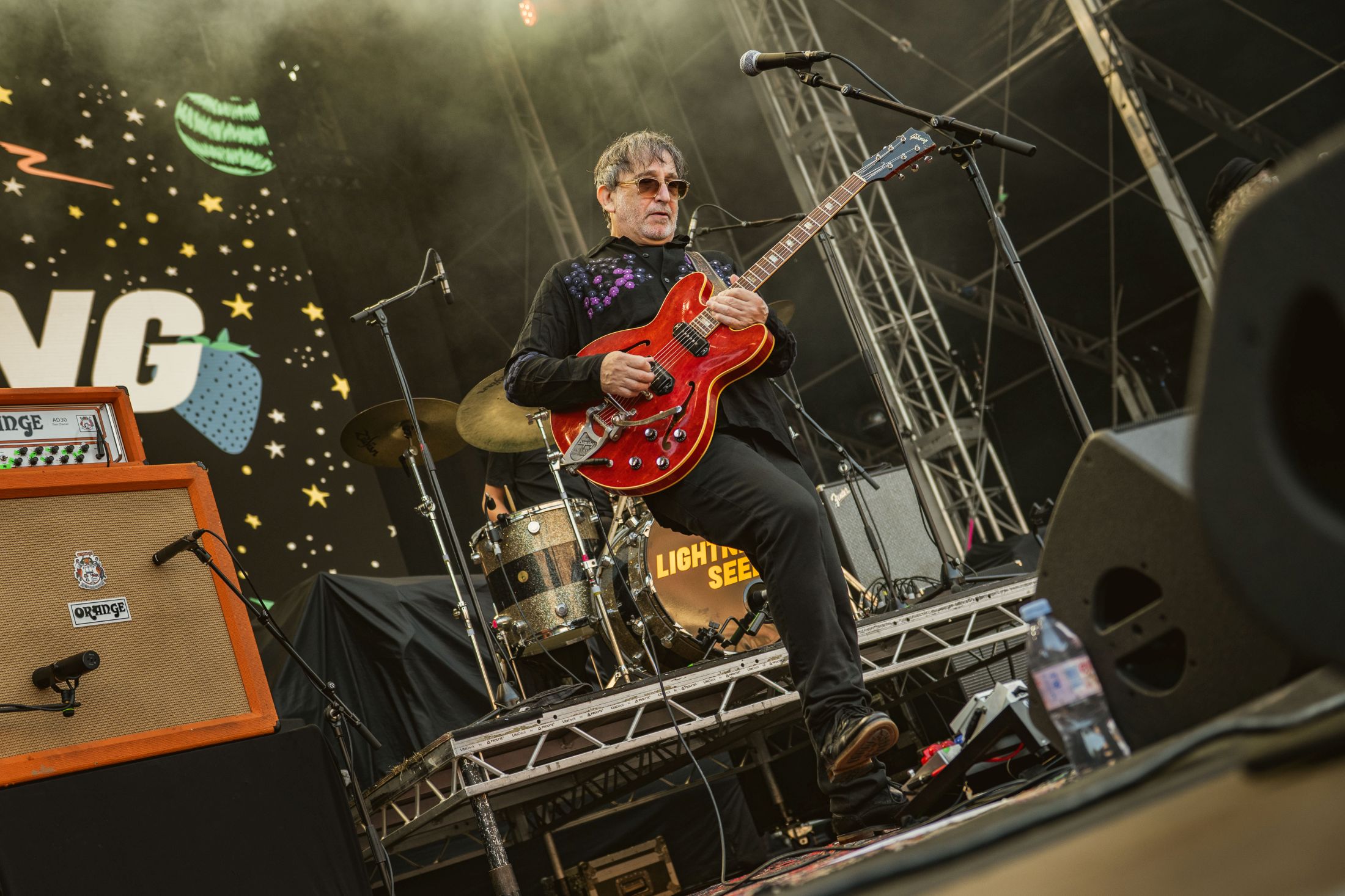 Guitarist performing on stage with red electric guitar at festival