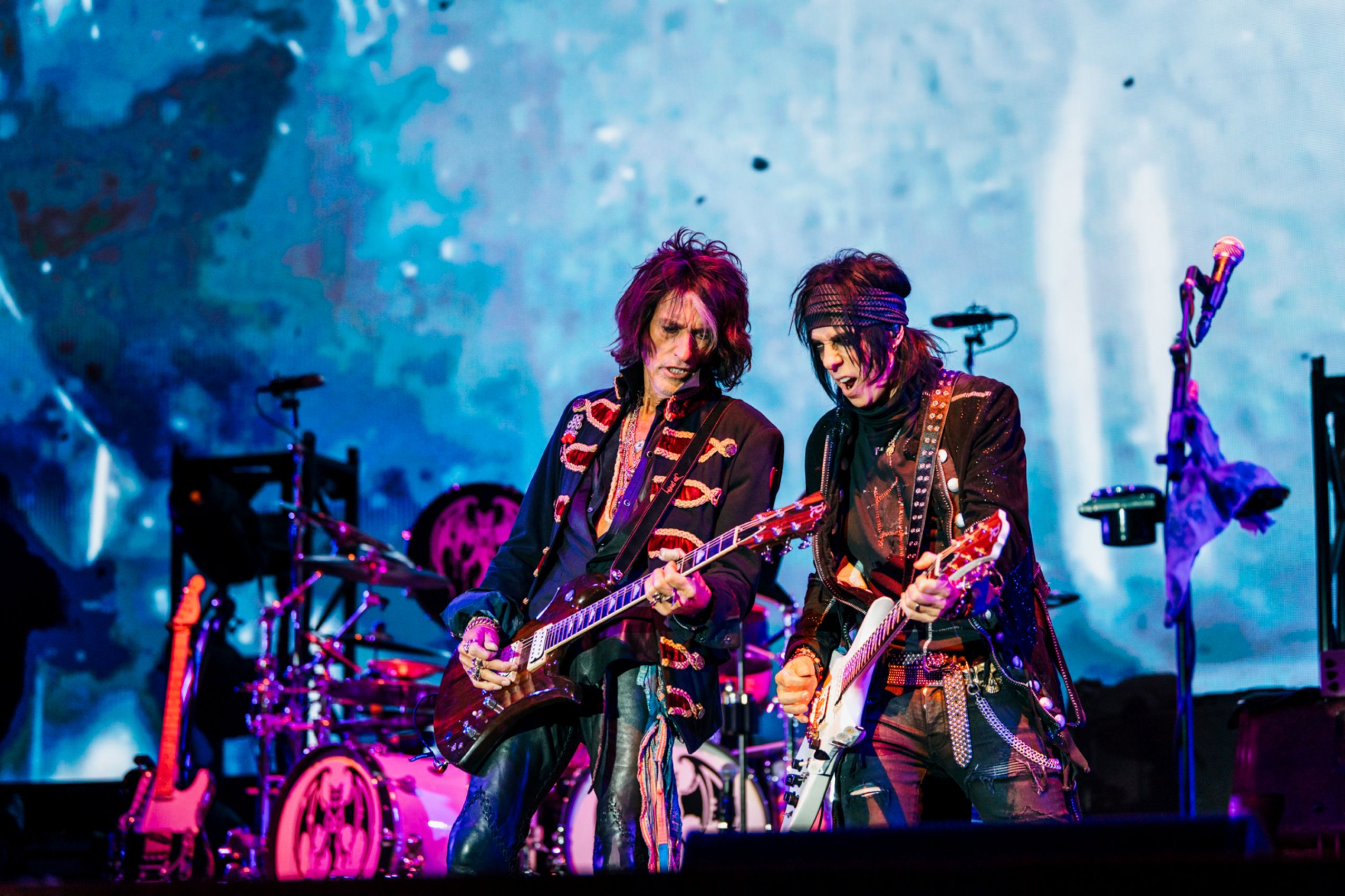 Two rock guitarists performing on stage with vibrant lighting