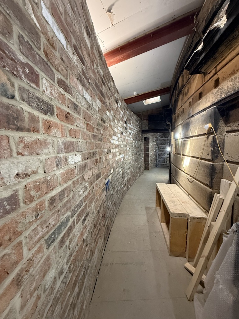 Curved brick corridor under construction with wooden bench