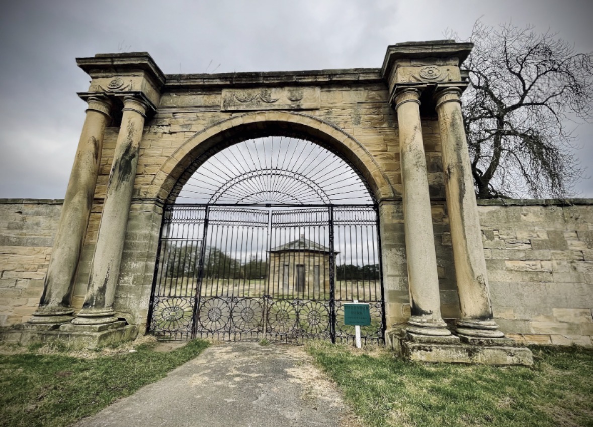 Historic stone archway with iron gate and distant pavilion