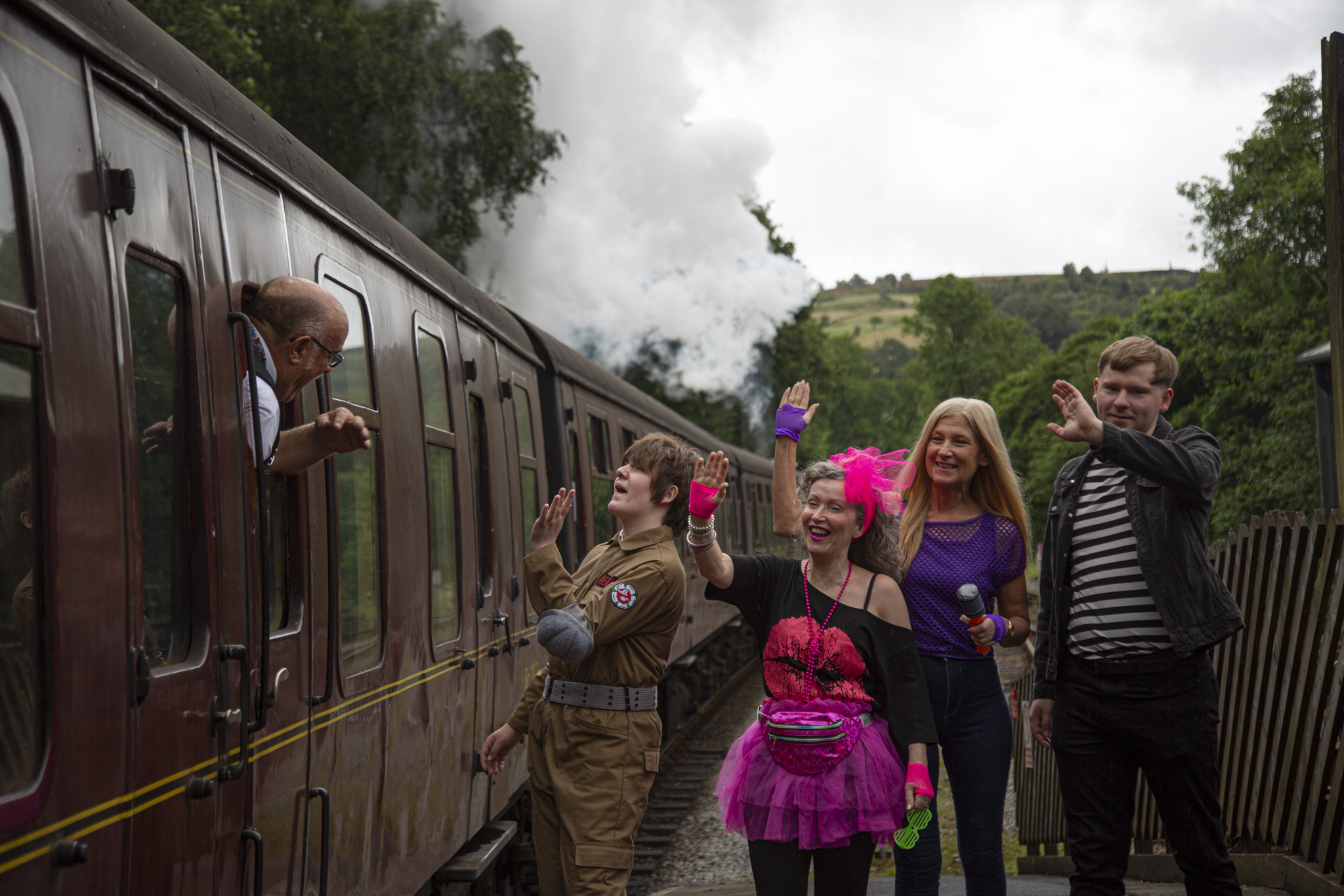 Group of people in costumes waving at steam train in countryside