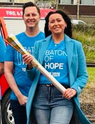 Smiling people in blue holding a ceremonial baton outdoors