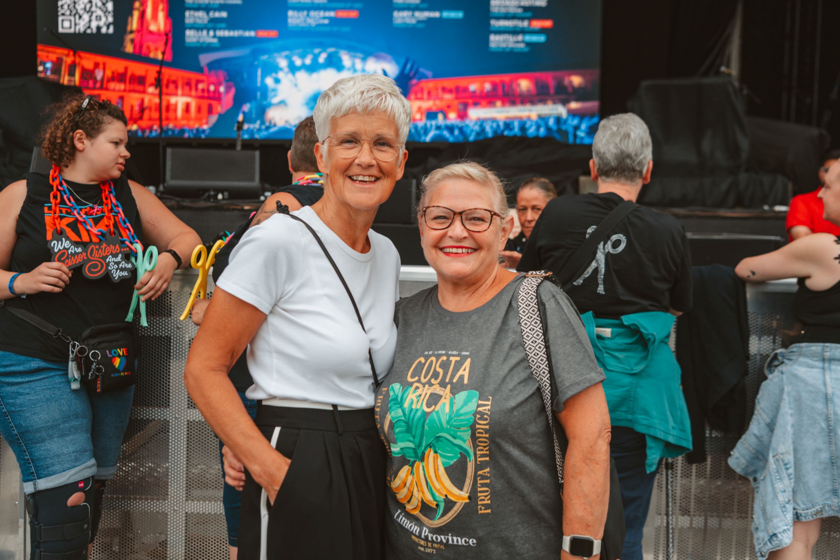 Two women smiling at an outdoor event with a stage backdrop