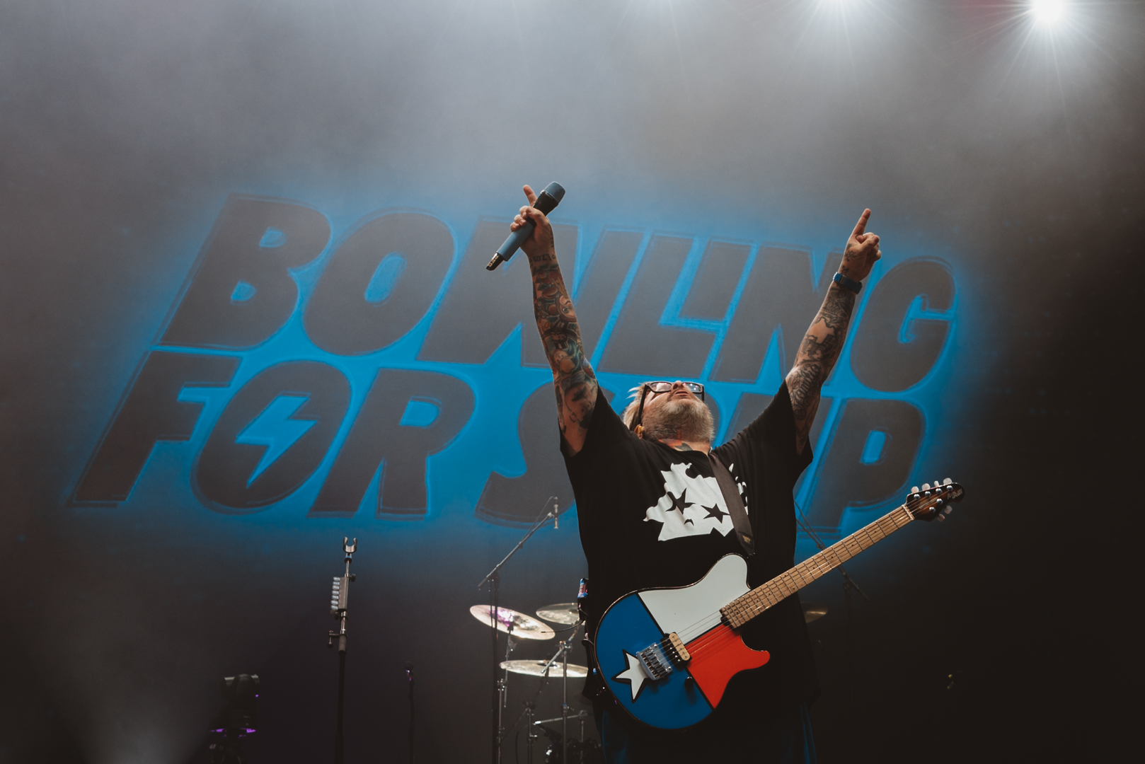 Musician on stage with guitar and arms raised under blue lights