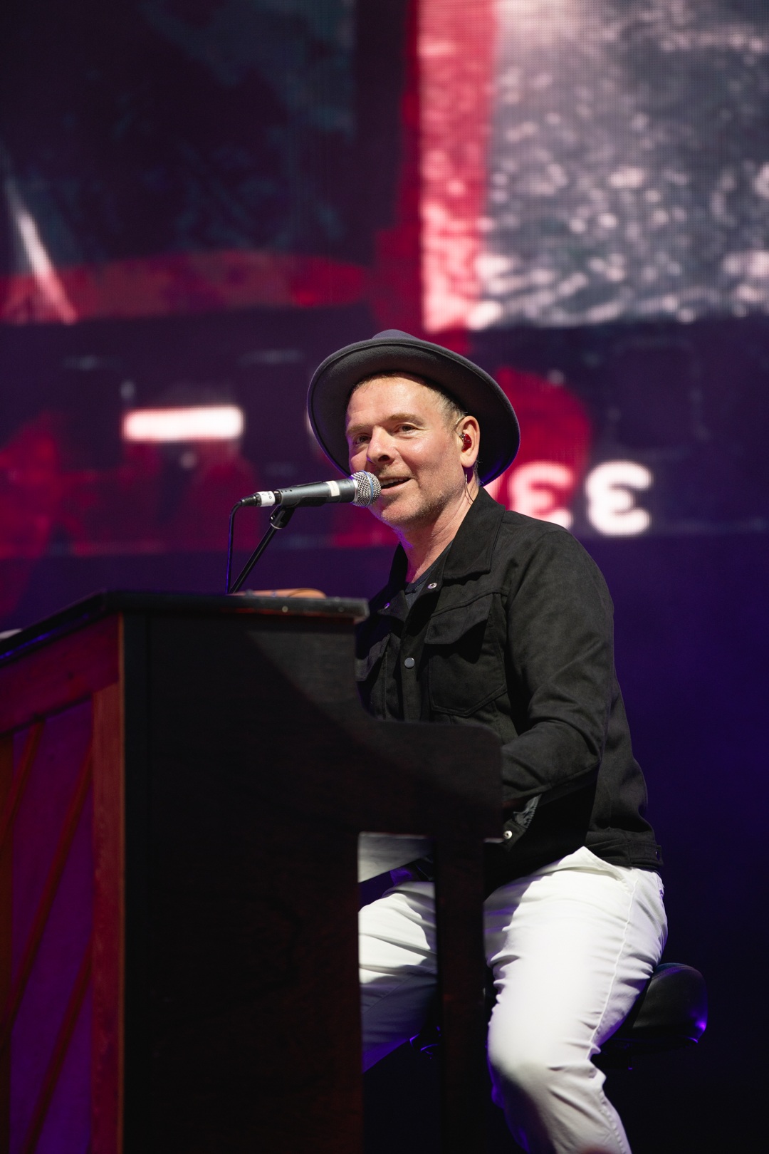 Musician in black jacket and hat playing piano on stage