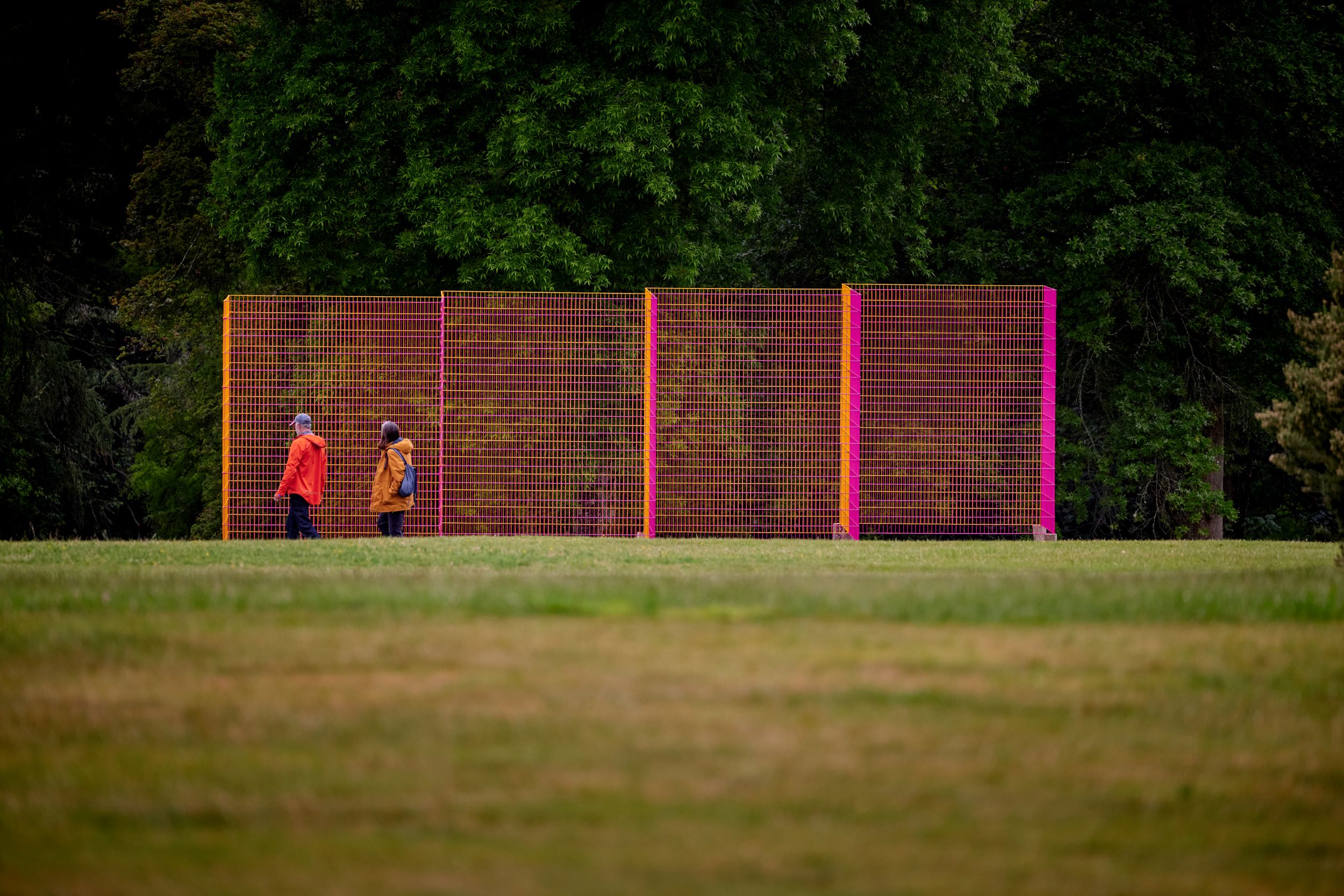 Two people walking by colourful temporary fencing in a park