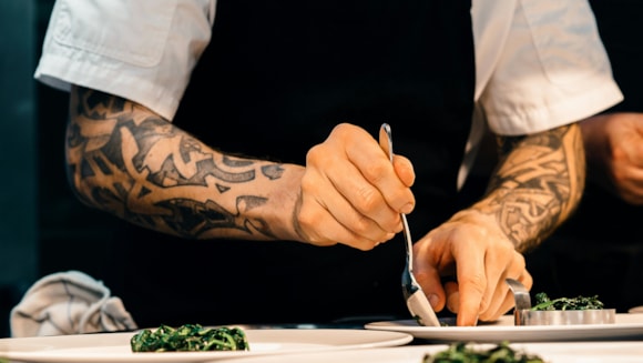 Chef with tattooed arms plating gourmet dish in kitchen