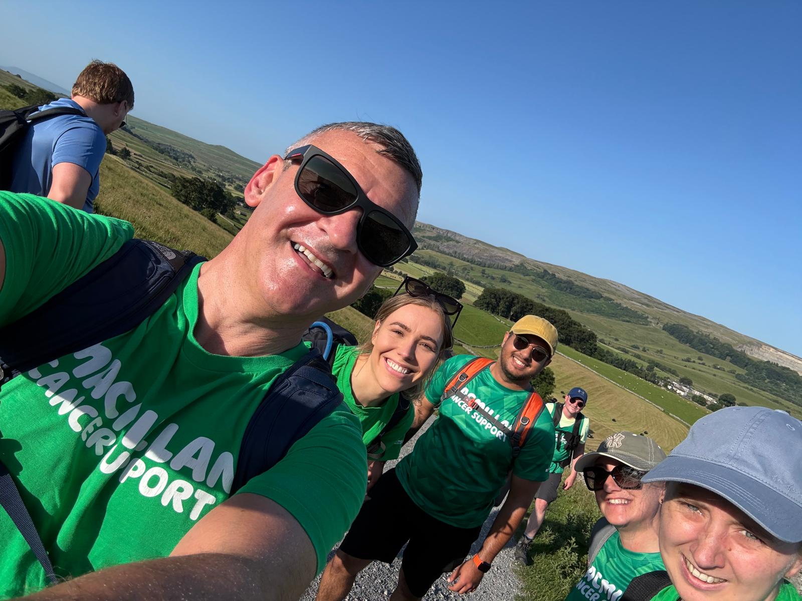 Group of hikers in green shirts smiling on a sunny hillside