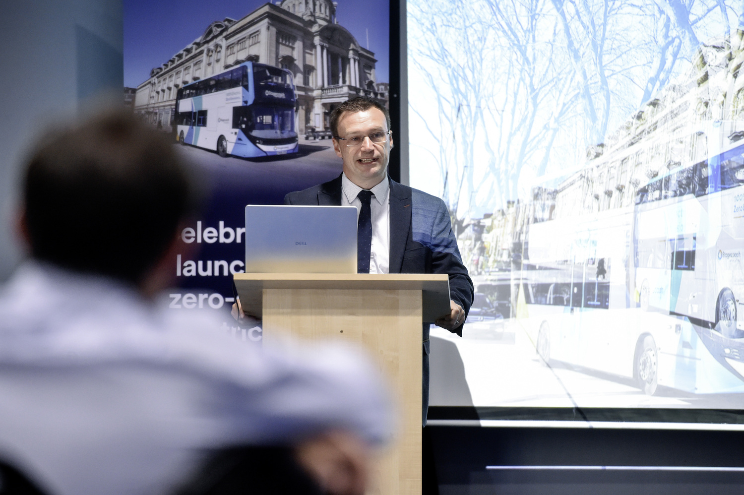 Man in suit presenting at podium with double-decker bus display