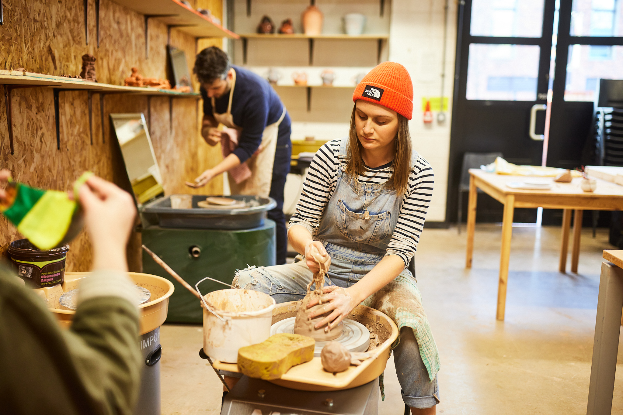 Young woman in orange hat sculpting clay in pottery class