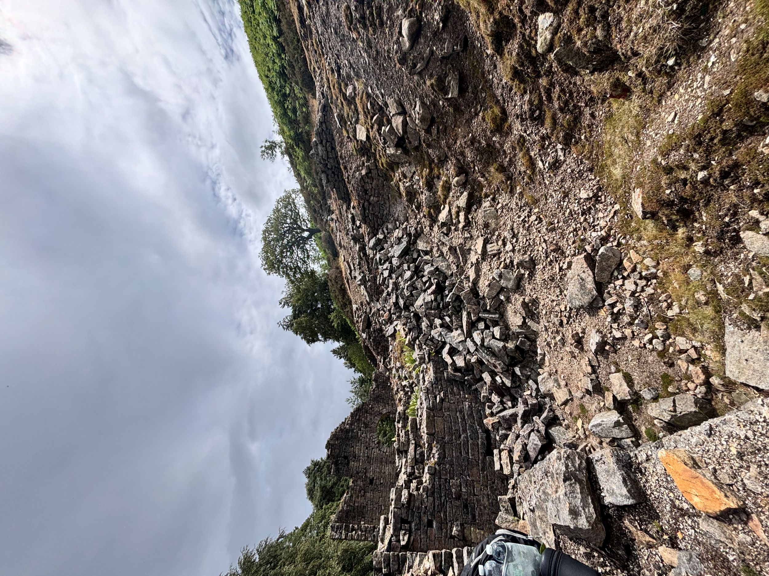 Ruins of ancient stone building on grassy hillside under cloudy sky
