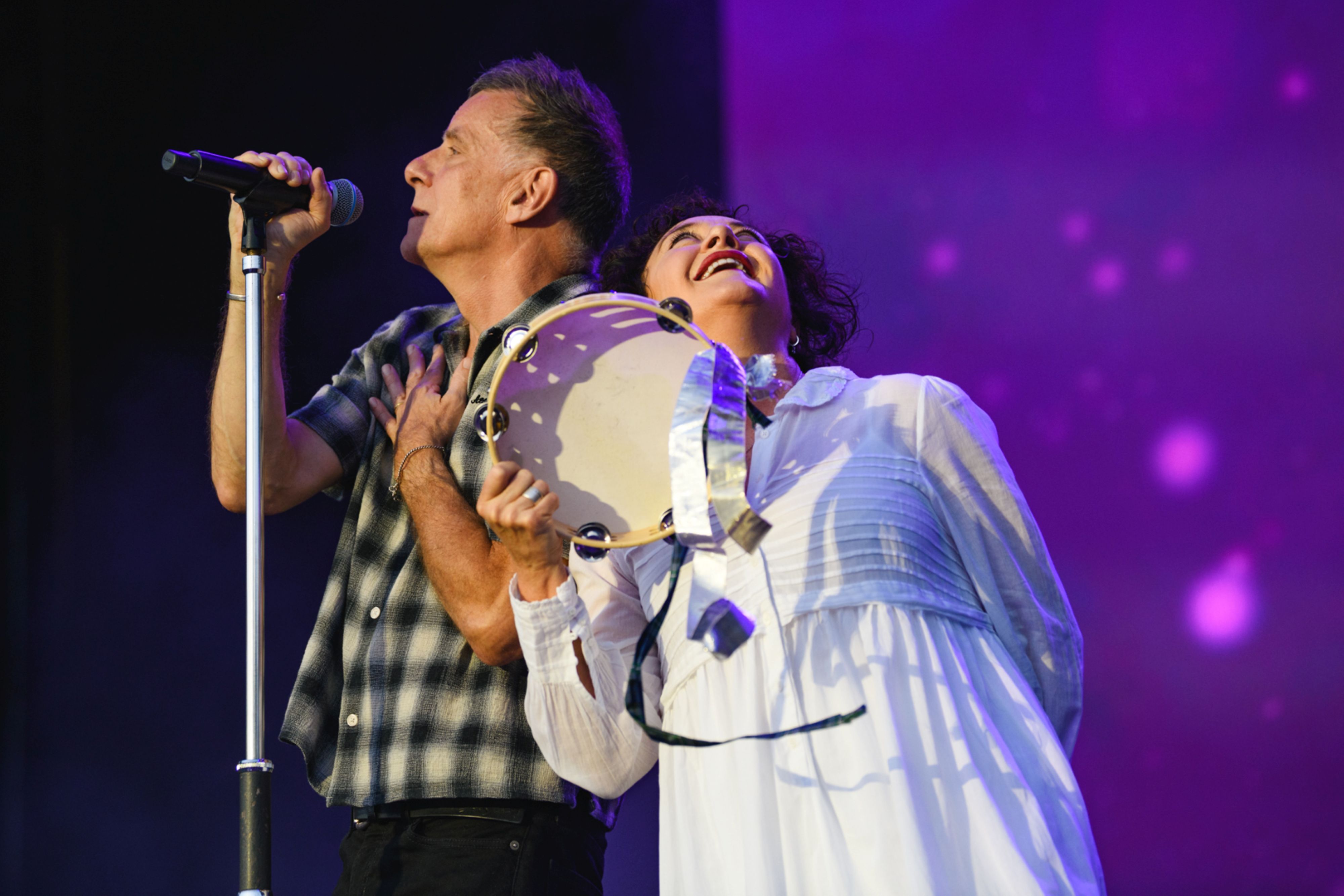 Two musicians performing on stage, one with tambourine