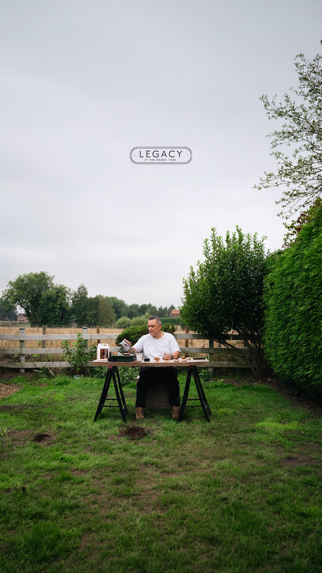 Man sitting at table in lush garden with overcast sky