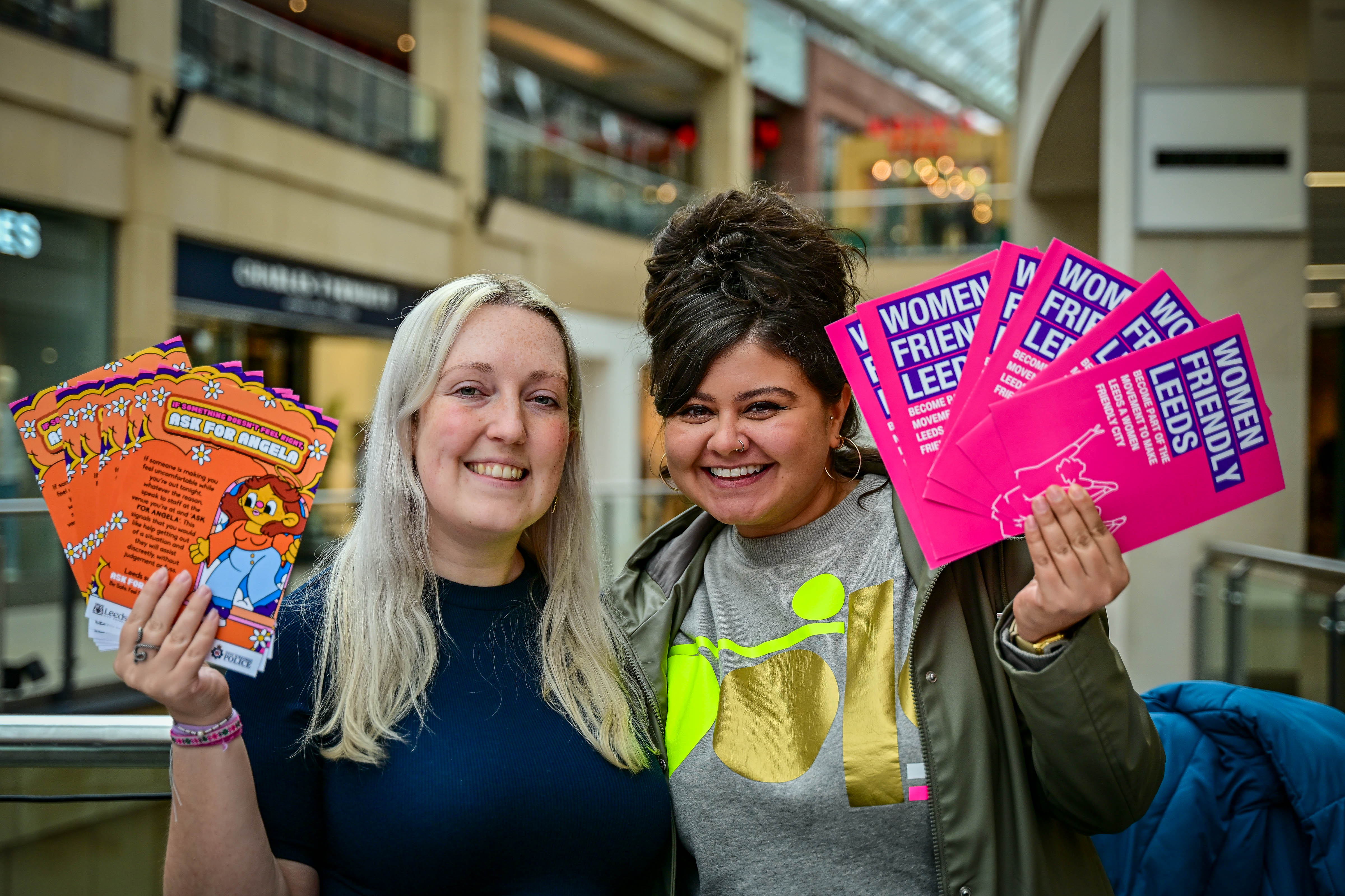 Two smiling women holding colourful brochures in a shopping centre