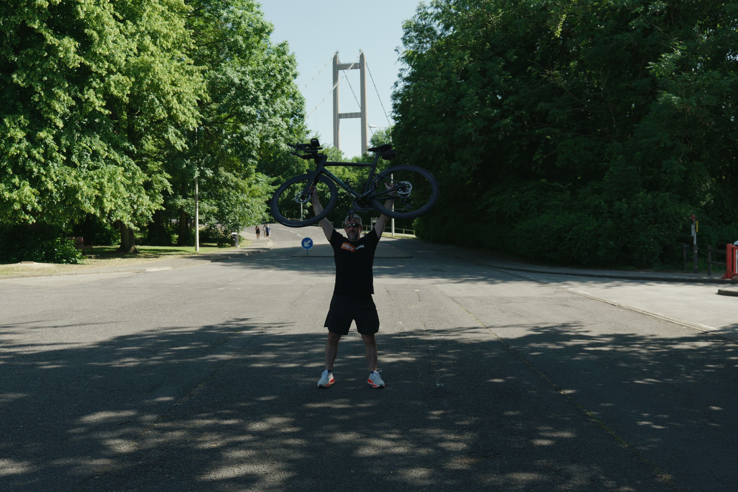 Cyclist lifting bike triumphantly on shaded road near bridge