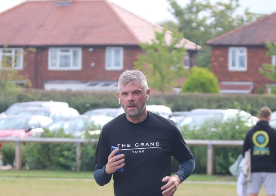 Man jogging on a field with houses and parked cars behind