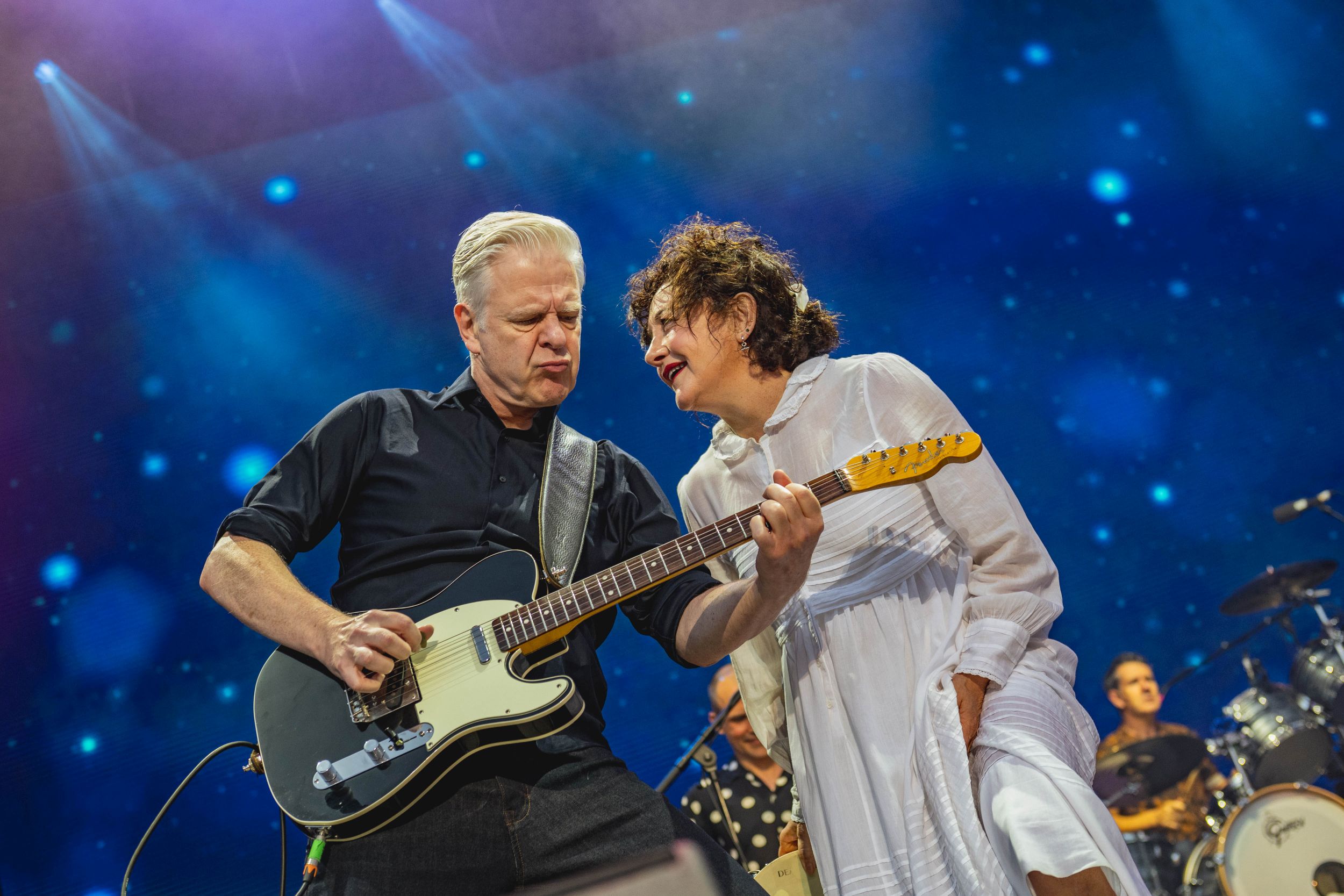 Musicians performing energetically on stage with guitar under blue lights