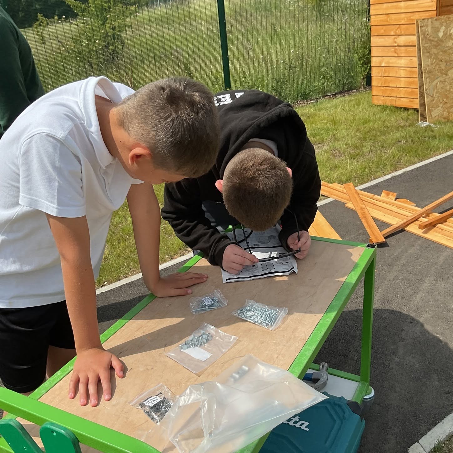 Children assembling wooden pieces on outdoor table in sunny garden