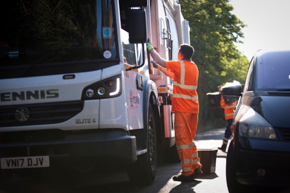 Refuse collectors in orange uniforms emptying bins into a lorry