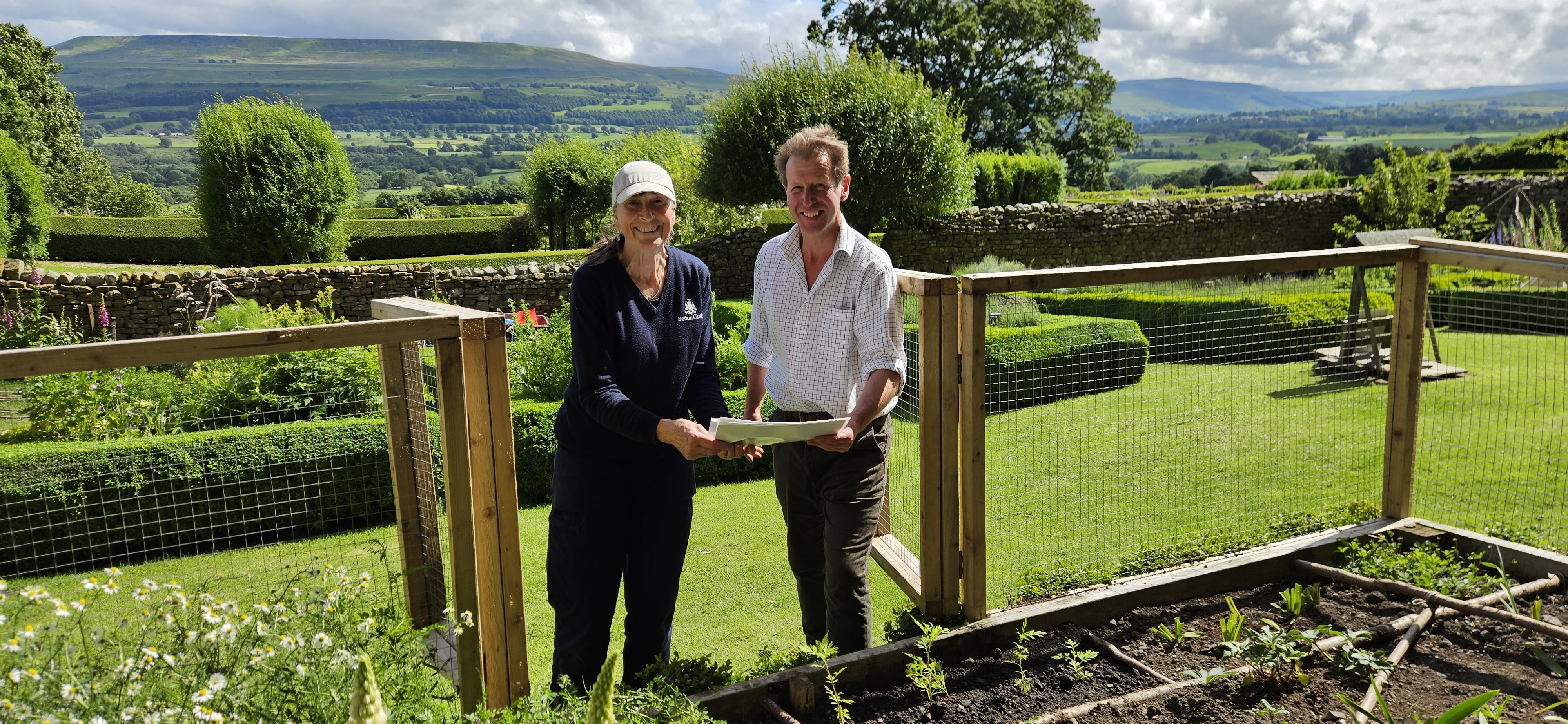 Couple standing in lush garden with rolling hills in background