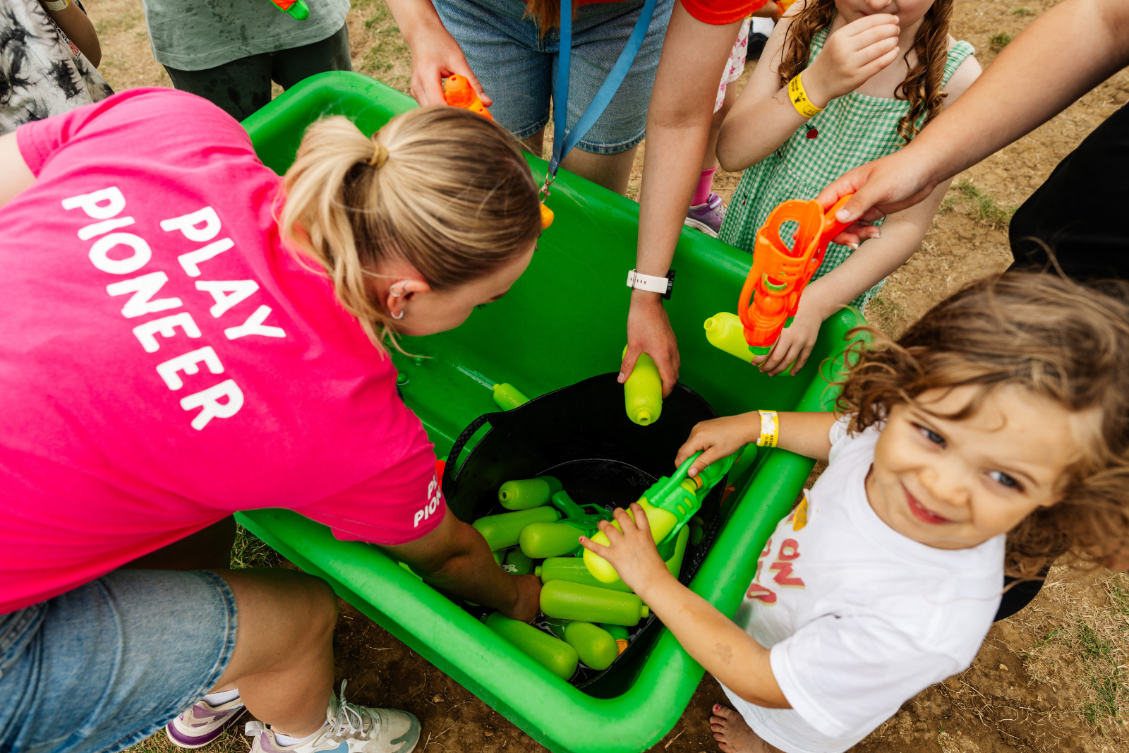 Children filling water pistols from a large green tub outdoors