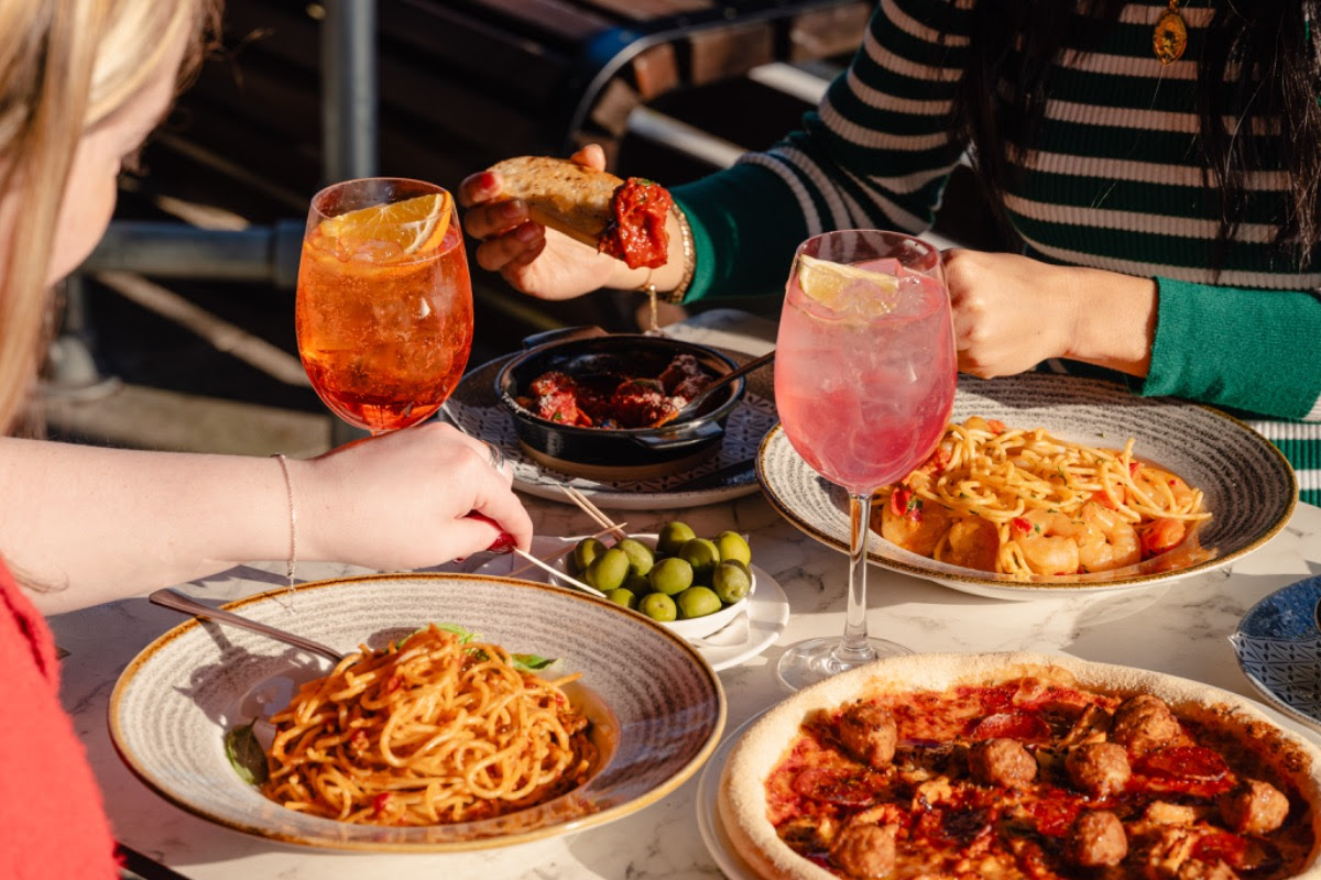 Outdoor dining scene with pasta, pizza, and cocktails