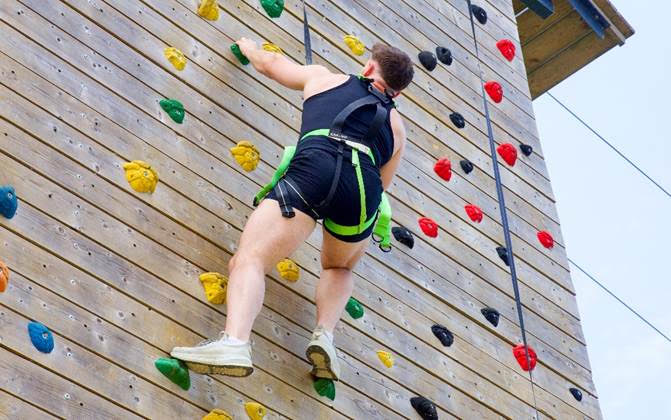 Person climbing outdoor wooden wall with colourful holds