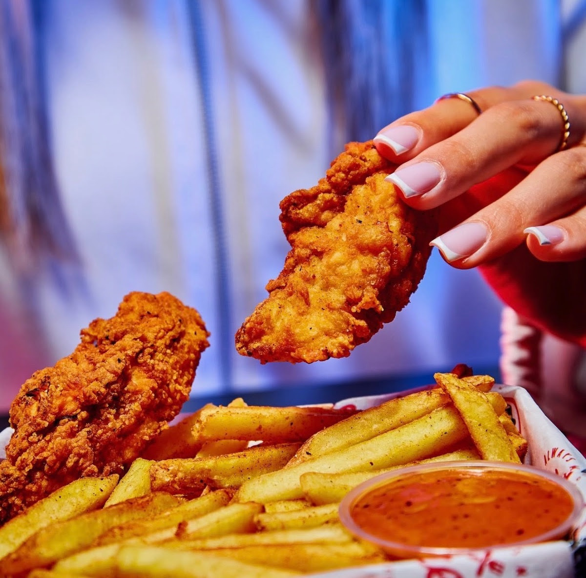 Close-up of hand holding crispy fried chicken with chips