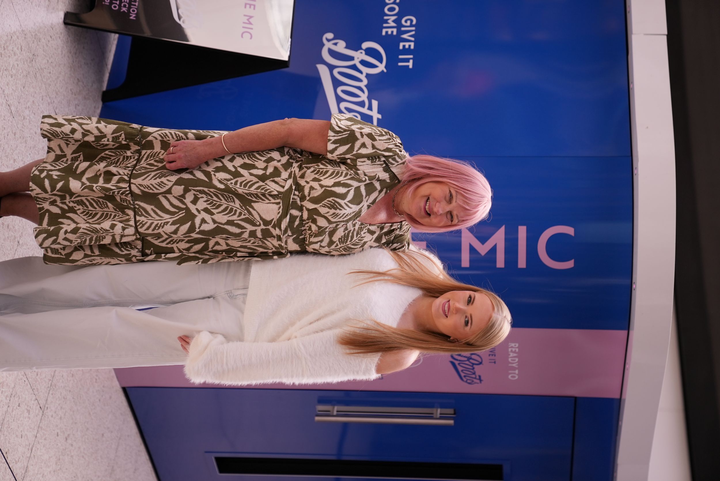 Two women smiling in front of a blue and pink Boots display