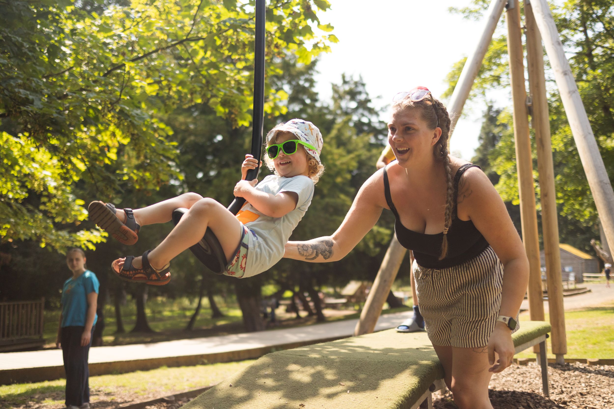 Child on swing with woman pushing in sunny park