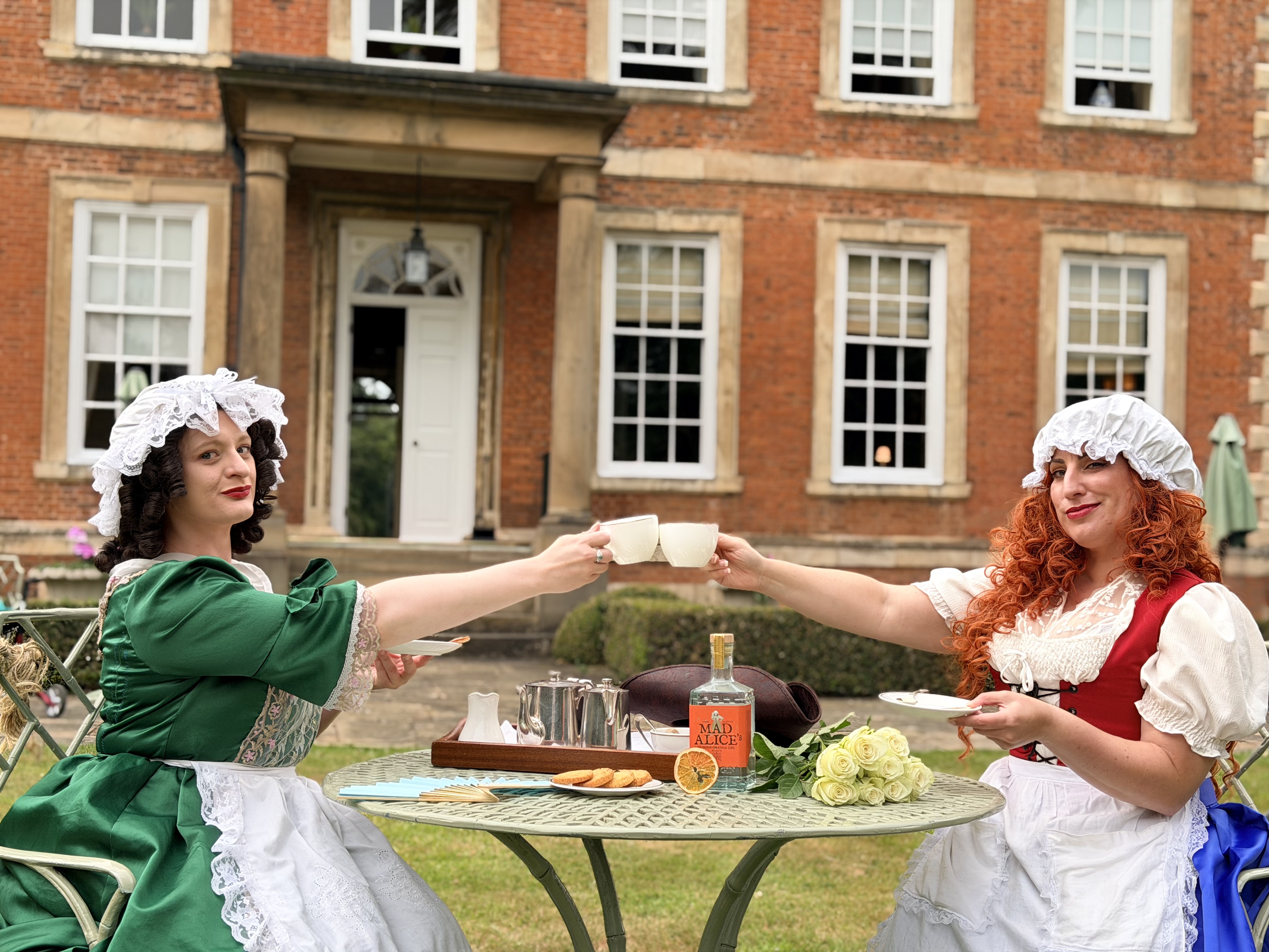 Two women in Victorian costumes enjoying tea outdoors