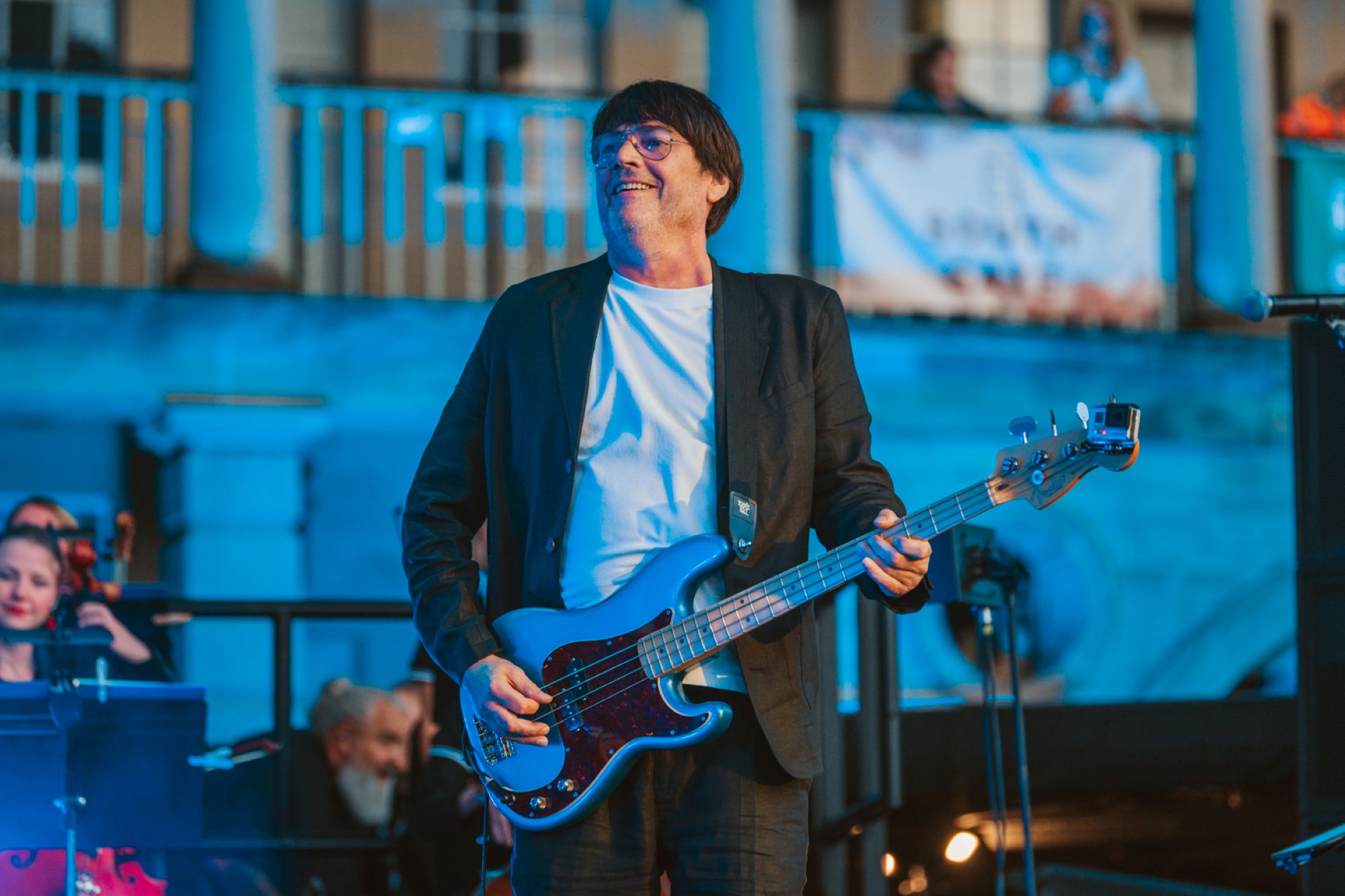 Musician playing bass guitar on outdoor stage with blue lighting