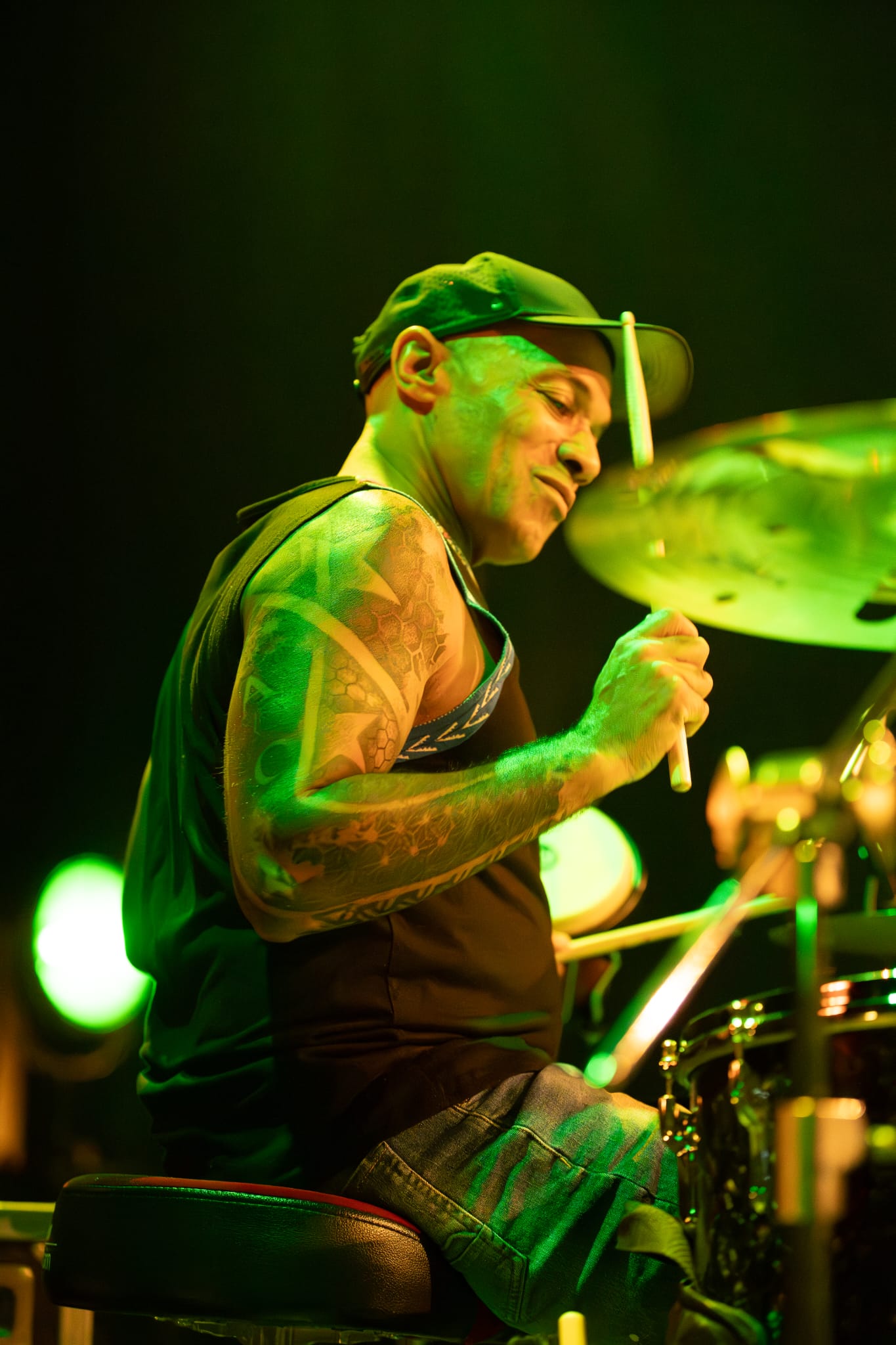 Drummer playing under green stage lights with tattoos visible