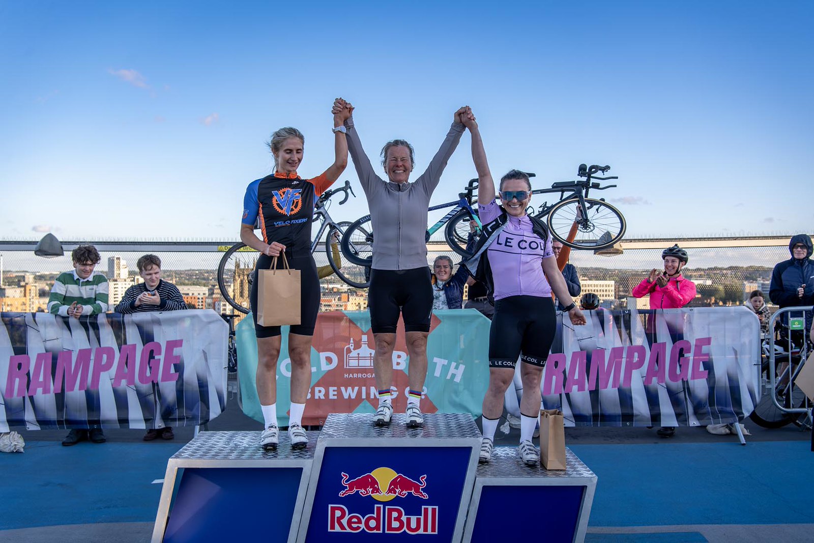 Cyclists on podium at outdoor event with cheering crowd