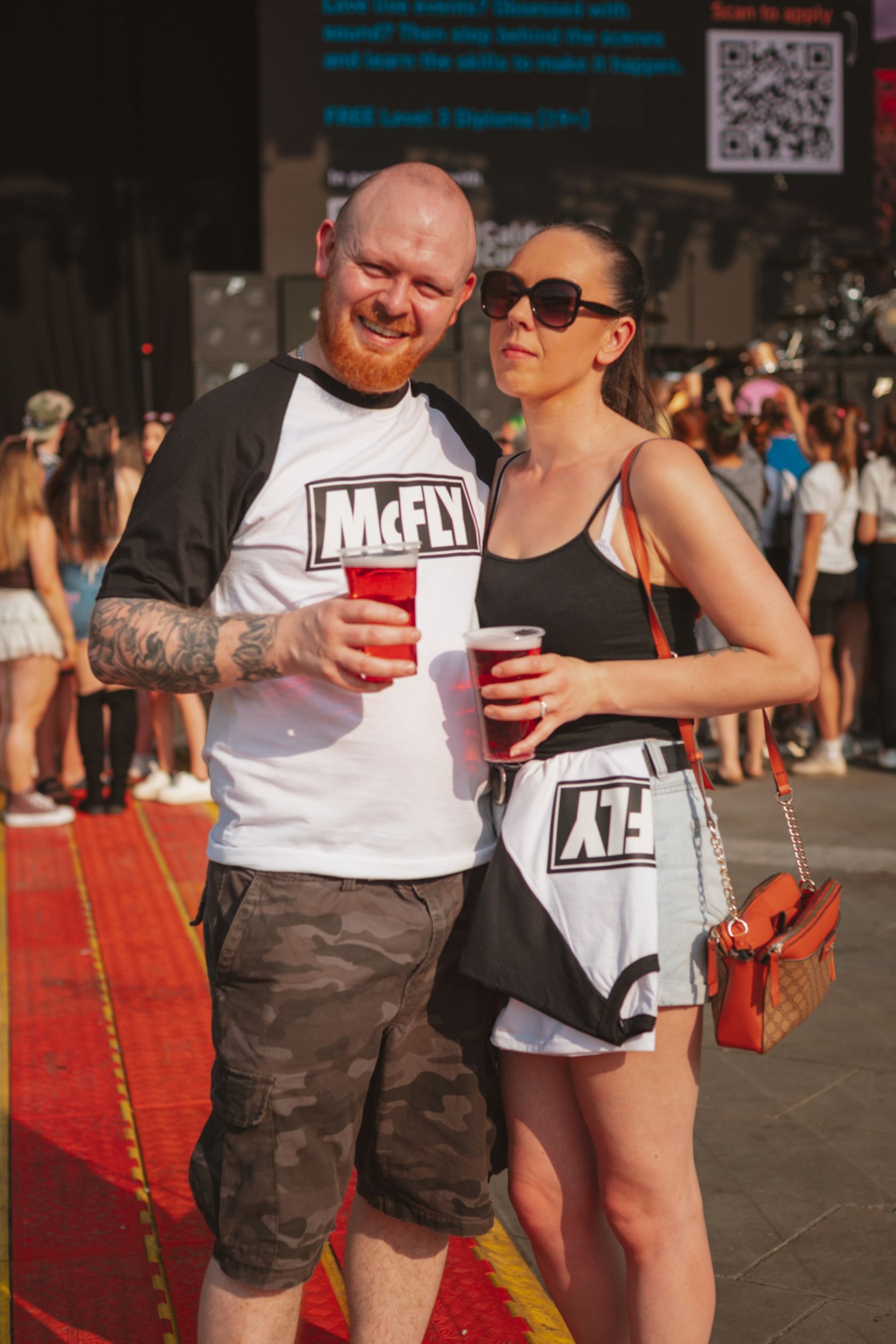Couple in casual attire holding drinks at outdoor festival