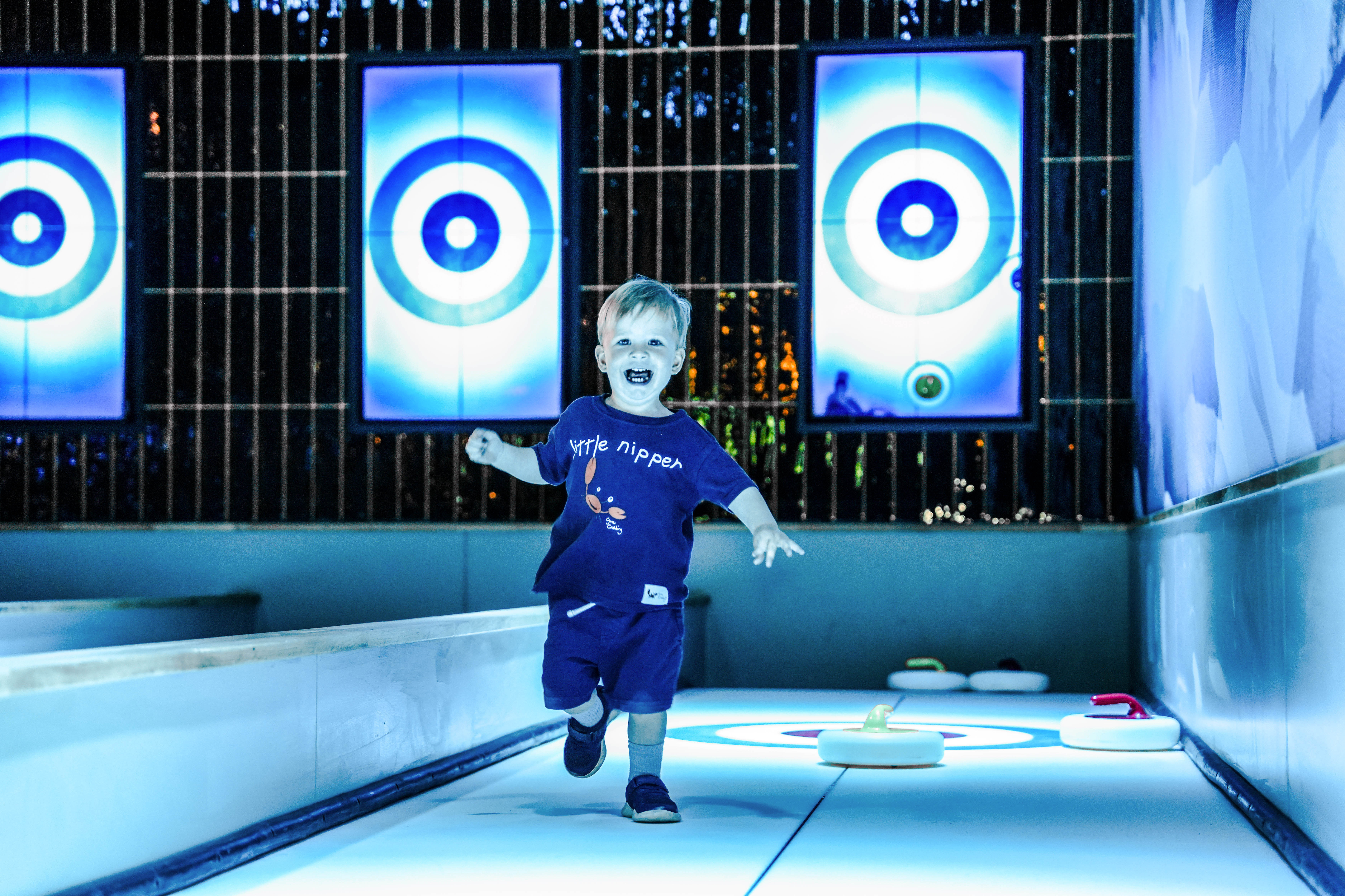 Child joyfully running on illuminated curling lane indoors
