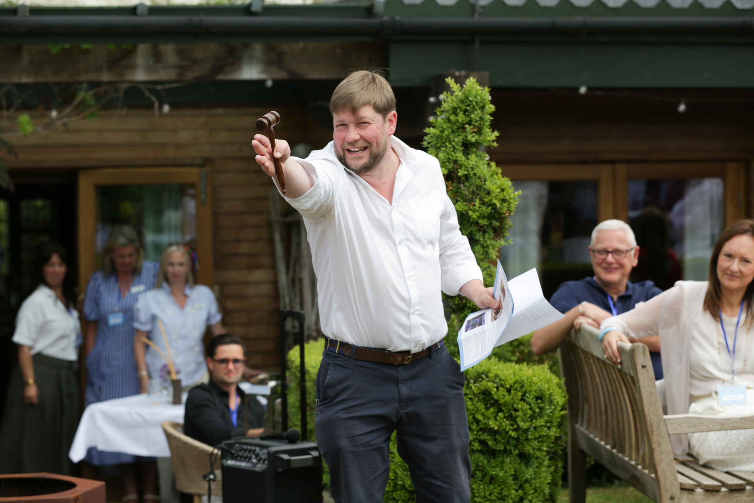 Auctioneer in a white shirt holding a gavel at an outdoor event